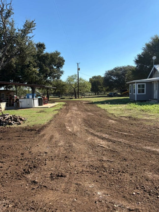 Dirt drive cut and graded between a covered patio and a house