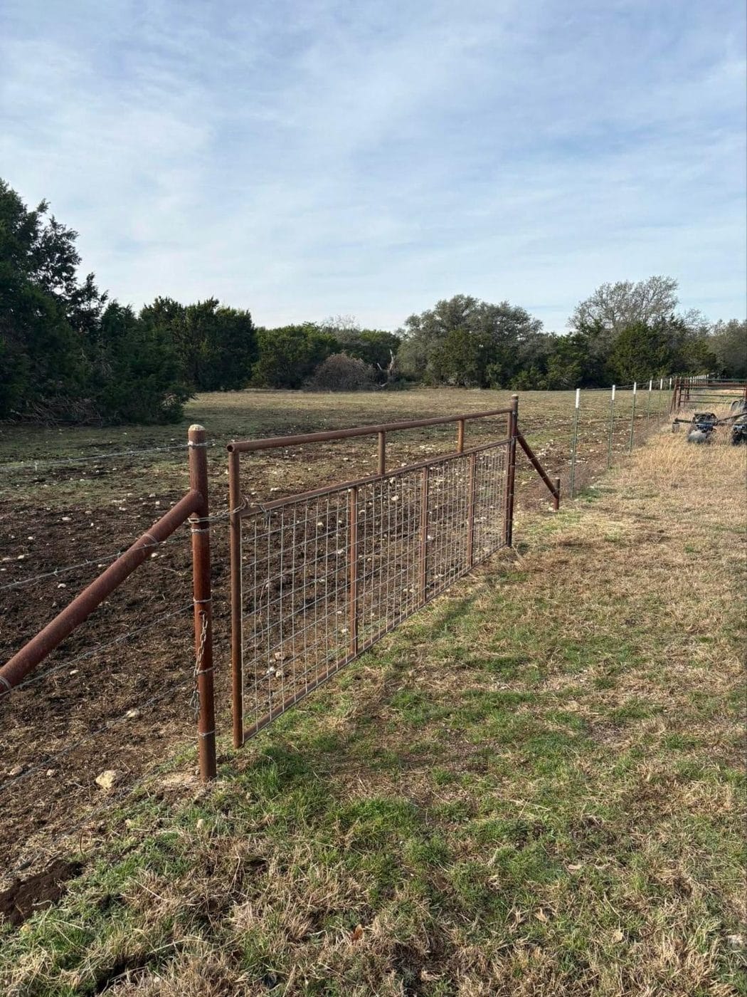 Pipe fence and gate along a pasture tree line